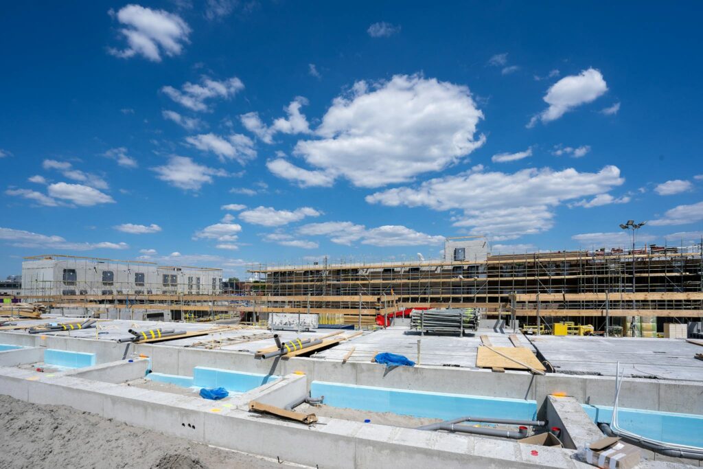 A contemporary construction site under a vibrant blue sky with visible scaffolding and concrete foundations.